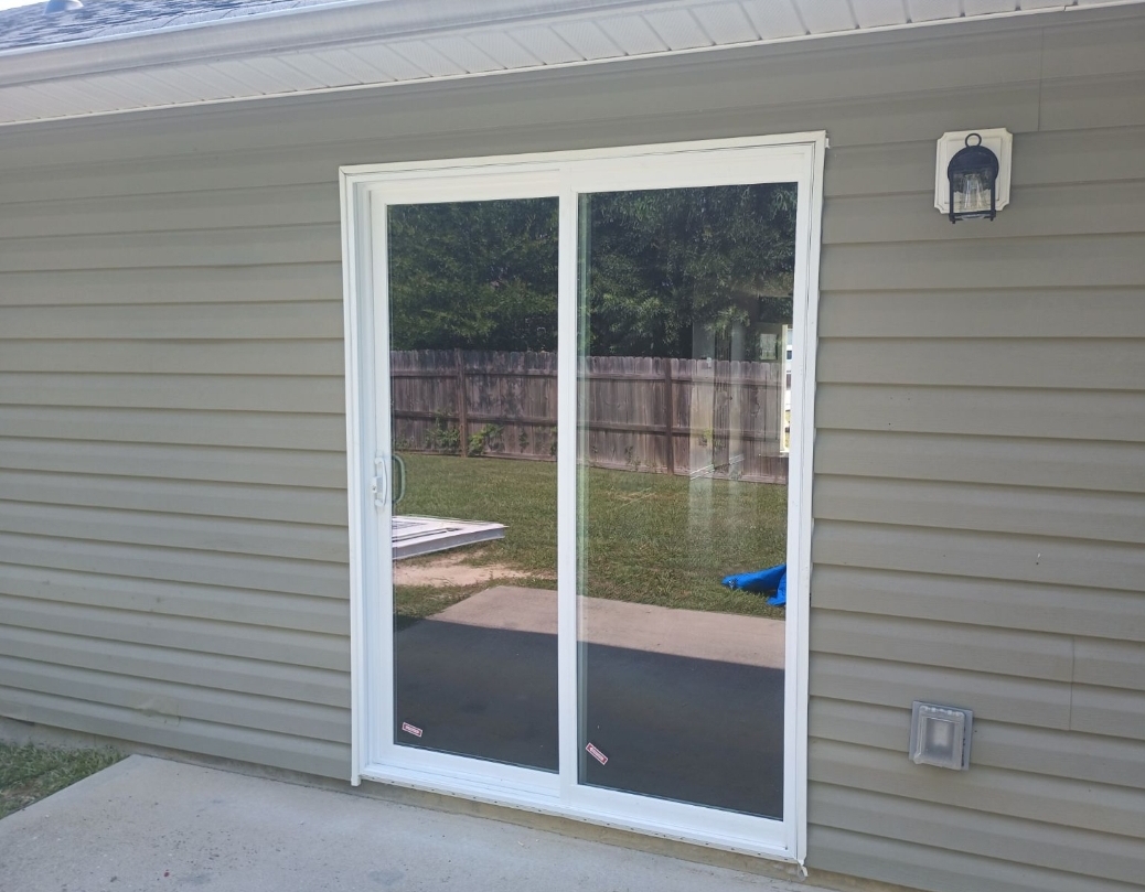 A new white sliding patio door installed in grey vinyl siding